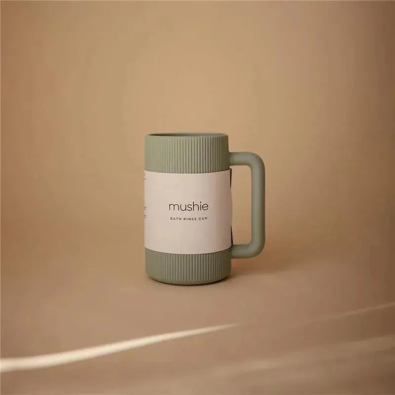 Sage green Mushie bath rinse cup with ribbed texture and a handle, displayed on a neutral background.