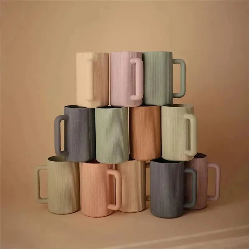 Mushie bath rinse cups in soft sage and various pastel colors stacked in a pyramid formation.