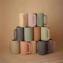 Mushie bath rinse cups in soft sage and various pastel colors stacked in a pyramid formation.