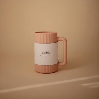 Mushie Bath Rinse Cup in blush color, featuring a ribbed design and a handle, displayed against a neutral background.