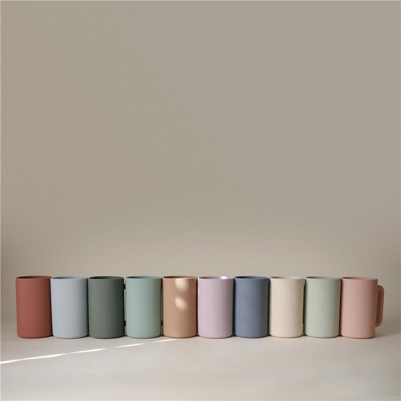 Mushie Bath Rinse Cup in Blush; a textured, pastel pink cup among a row of colorful rinse cups.