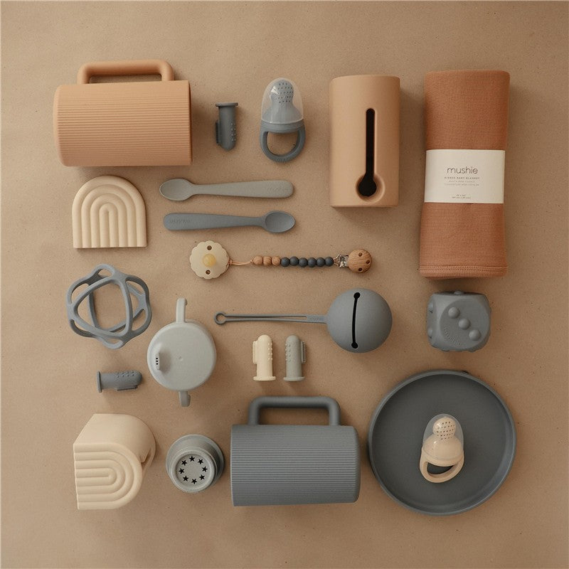 Mushie Bath Rinse Cup in natural colors, accompanied by various silicone utensils and bath accessories on a neutral background.