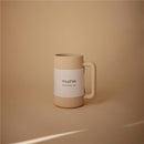 Mushie bath rinse cup in shifting sand color, featuring ribbed design and a white label with brand name and product details.