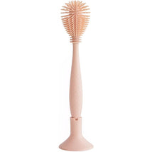 Mushie Silicone Baby Bottle Brush in blush color, featuring a textured handle and a rounded cleaning head stored in a holder.