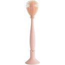 Mushie Silicone Baby Bottle Brush in blush color, featuring a textured handle and a rounded cleaning head stored in a holder.