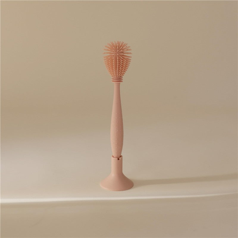 Mushie silicone baby bottle brush in blush color, featuring a sleek handle and a textured brush head for effective cleaning.