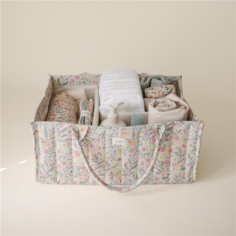 Mushie Baby Diaper Caddy in Pastel Blooms design, filled with diapers, wipes, cream, and clothes, organized for newborn essentials.