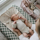 Newborn lying on a changing pad with a pastel blooms diaper caddy nearby, holding its hands and looking up.