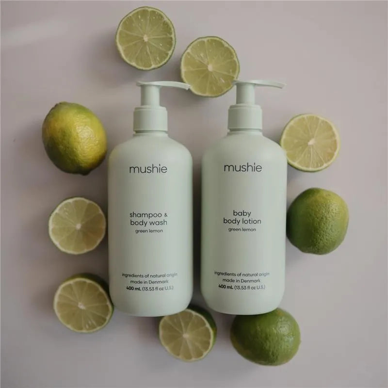 Baby lotion and shampoo bottles by Mushie in green lemon scent, surrounded by fresh lime halves.