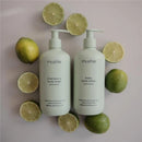 Baby lotion and shampoo bottles by Mushie in green lemon scent, surrounded by fresh lime halves.