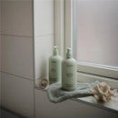 Two Mushie baby care products, a green lemon baby lotion and shampoo & body wash, are displayed on a windowsill with a soft towel.