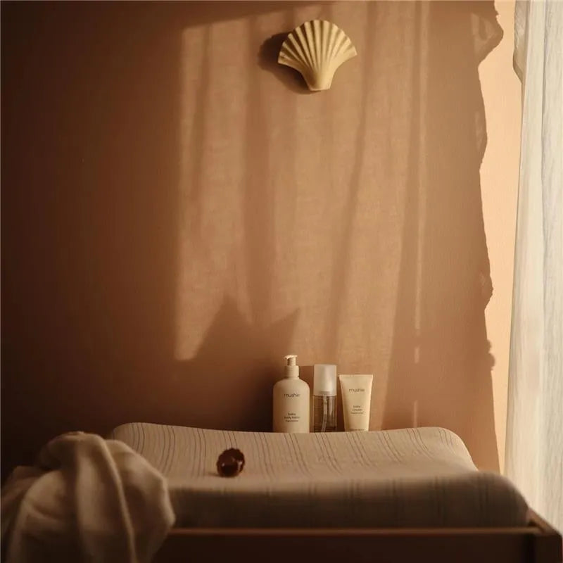 Mushie Baby Organic Body Lotion and related skincare products displayed on a soft surface in warm, natural light.