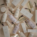 Mushie Baby Organic Body Lotion in a lavender bottle among various other baby care products on a neutral background.