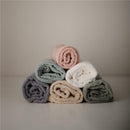 Hooded towels neatly rolled and stacked in soft colors: sea mist green, pink, white, beige, and gray.