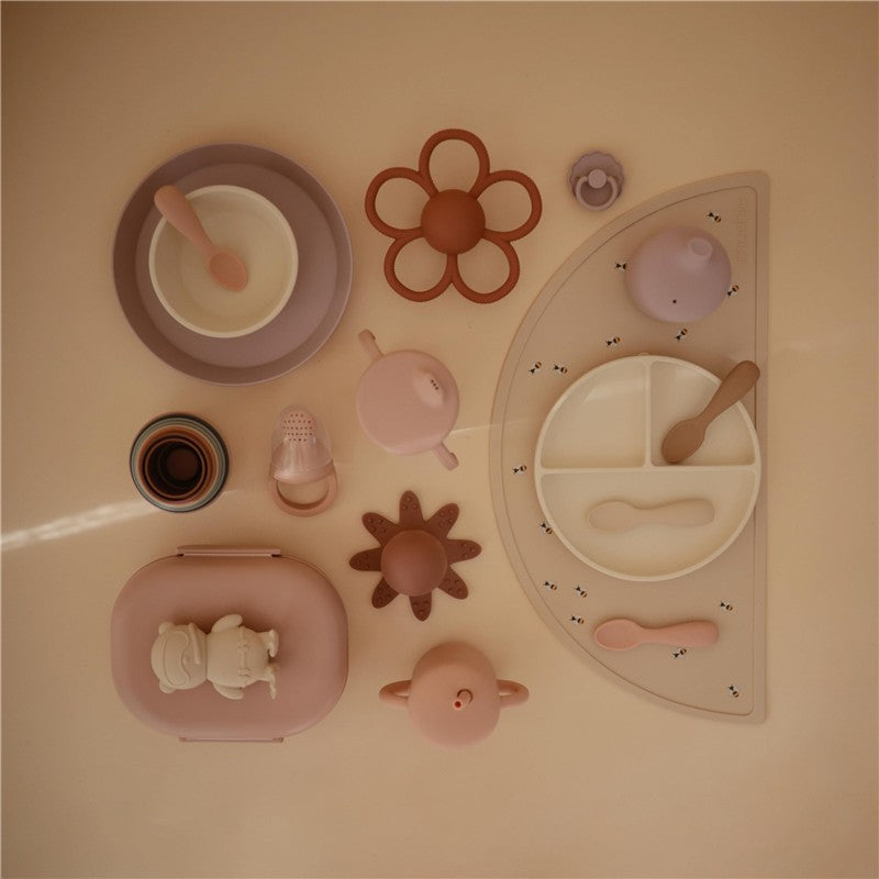 Mushie Bento Lunch Box in blush color, surrounded by various pastel tableware, including plates, cups, and utensils.