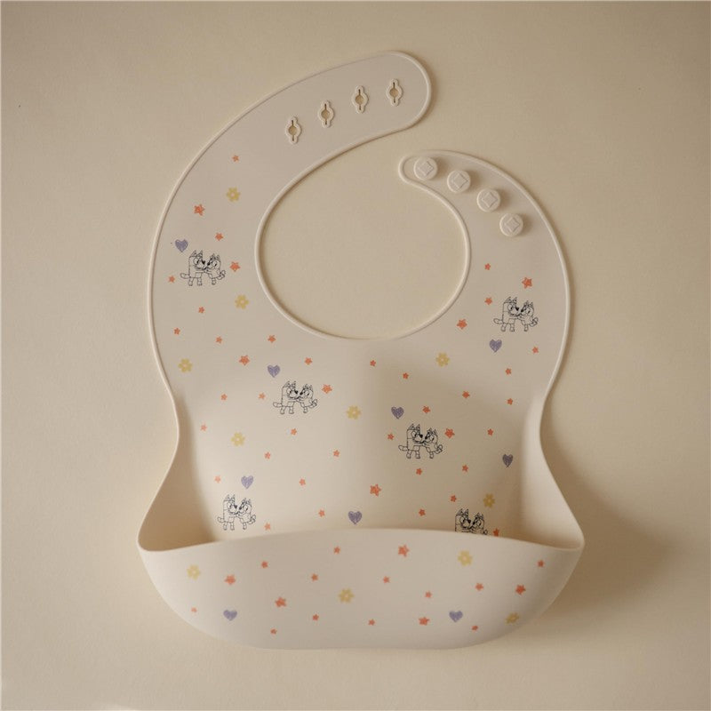 Silicone baby bib in ivory with colorful star and heart patterns, featuring adjustable snap buttons.