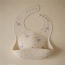 Silicone baby bib in ivory with colorful star and heart patterns, featuring adjustable snap buttons.