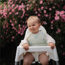 Silicone baby bib in blue with cartoon designs, worn by a seated baby in a high chair, surrounded by pink flowers.