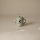 Mushie Silicone Training Cup in Bluey Sage with a blue cartoon dog design and a straw.
