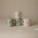 Bluey X Mushie snack cups in sage and neutral colors, featuring fun cartoon designs of Bluey and friends, stacked together.