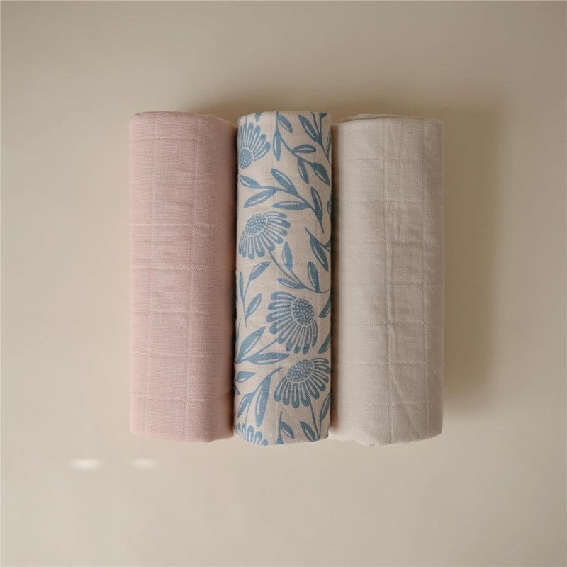 Three rolled changing pad liners in pink, floral blue, and cream, showcasing soft fabric texture and patterns.