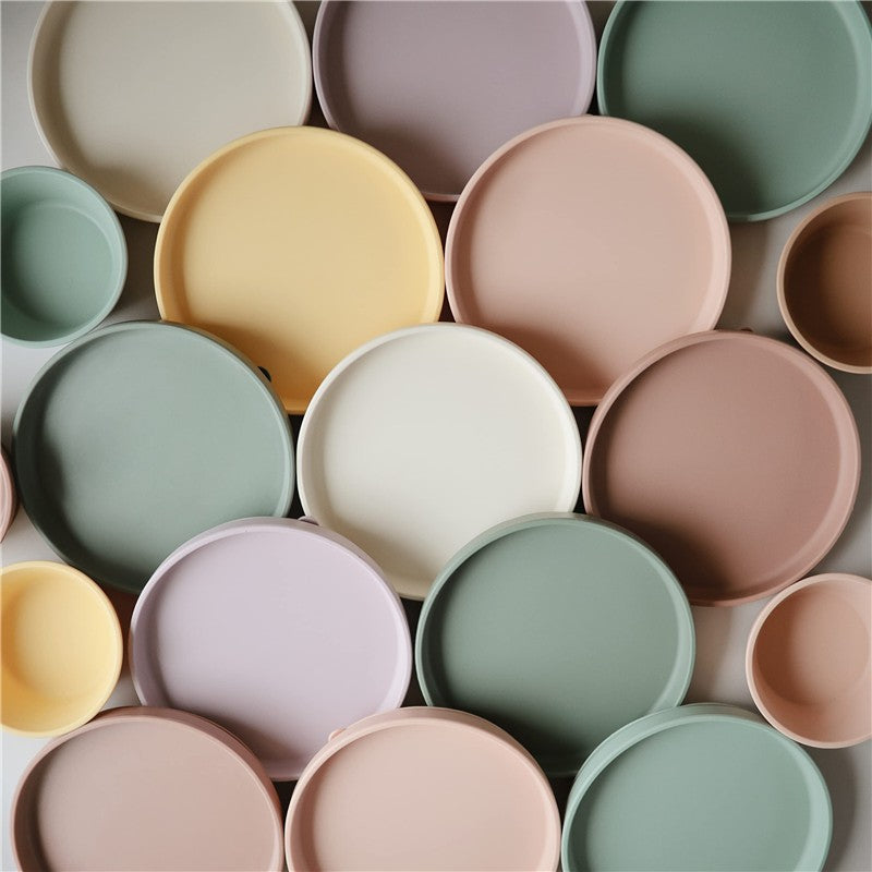 Various silicone suction plates in pastel colors, showcasing the Mushie Classic collection, including blush tones.