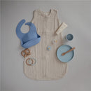 Classic silicone suction plate in powder blue, surrounded by a sleep sack, teething toys, and baby care items.