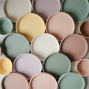 Mushie Classic Silicone Suction Plates in powder blue, arranged with various pastel-colored plates of different sizes.
