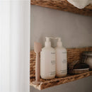 Mushie silicone diaper cream applicator next to shampoo and body wash bottles on a woven shelf.