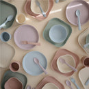 Blush Mushie silicone dinnerware set including fork and spoon, featuring various plates and bowls in soft pastel colors.