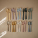Silicone fork and spoon set in various pastel colors arranged on a neutral background, designed for toddlers.
