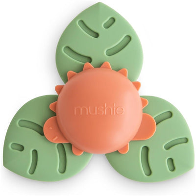 Mushie Dino Suction Spinner Toy features a green leaf base with a central orange spinning dinosaur design, ideal for bath and play.
