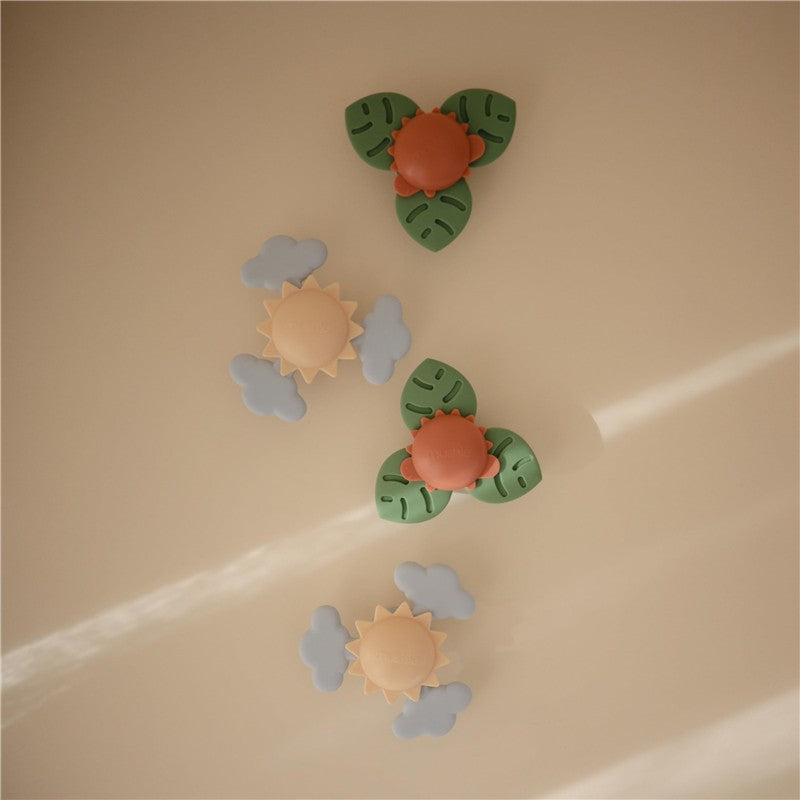 Four colorful suction toys featuring a dinosaur face, sunny flowers, and clouds, designed for bath play.