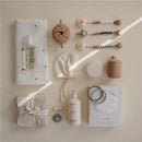 Mushie Eva Pacifier Clip in a cloud design featured among baby essentials including a muslin swaddle, oil, and body lotion.