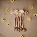Mushie Eva Pacifier Clip in mauve with wooden beads and a floral pacifier holder, surrounded by yellow paper flowers.
