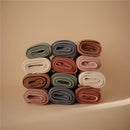 Soft baby blankets arranged in a stack, showing various colors including ivory, terracotta, and sage green.