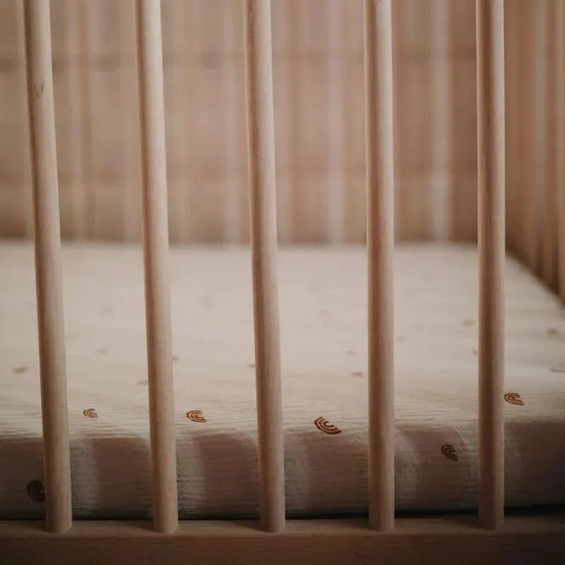 Extra soft muslin mini crib sheet with a subtle pattern, placed in a wooden crib with vertical slats.