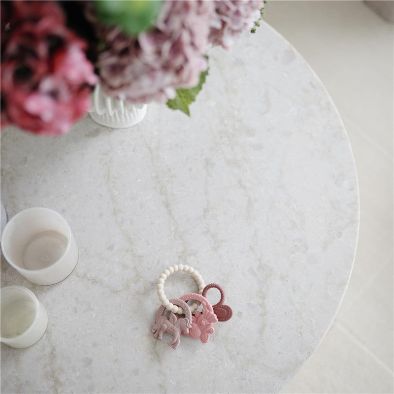 Mushie Fairy Teething Ring on a marble table, featuring pastel-colored silicone animal shapes and a beaded handle.