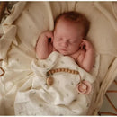 Sleeping baby swaddled in a light blanket with a natural rubber pacifier in blush and cream colors.