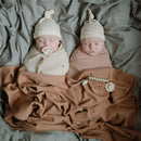 Two sleeping babies swaddled in different colored blankets, one using a Mushie Silicone Pacifier Clip in stone.