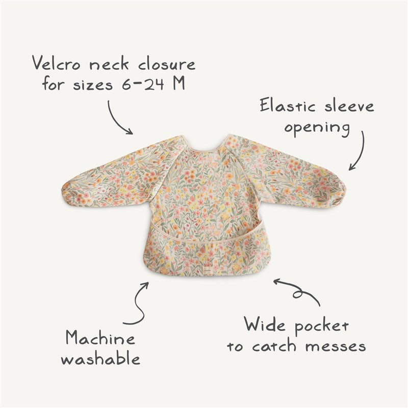 Mushie Long Sleeve Bib in Blush with floral design; features Velcro neck closure, elastic sleeve openings, and wide pocket.