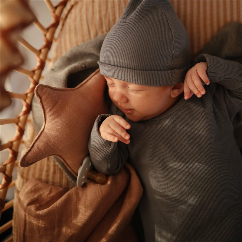 A sleeping baby in a gray outfit and hat rests on a cozy blanket, cradling a star-shaped plush toy.