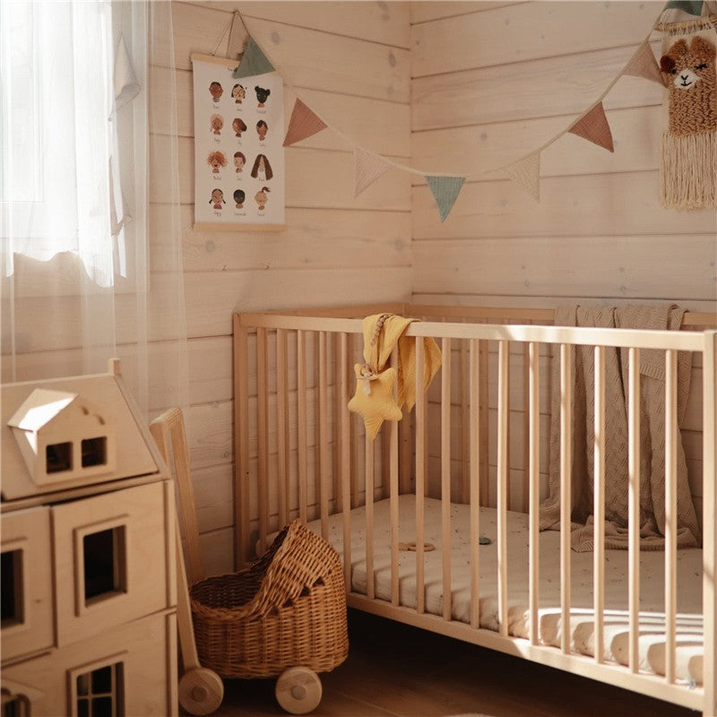 Mushie Star Lovey in Fall Yellow placed in a crib with hanging fabric and a decorative garland in a cozy nursery setting.