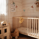 Mushie Star Lovey in Fall Yellow placed in a crib with hanging fabric and a decorative garland in a cozy nursery setting.
