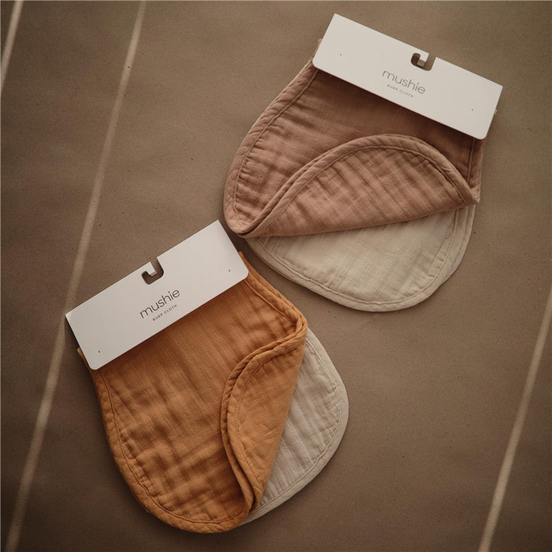 Mushie Organic Cotton Muslin Burp Cloths 2-Pack in blush and fog colors, displayed folded with hang tags.