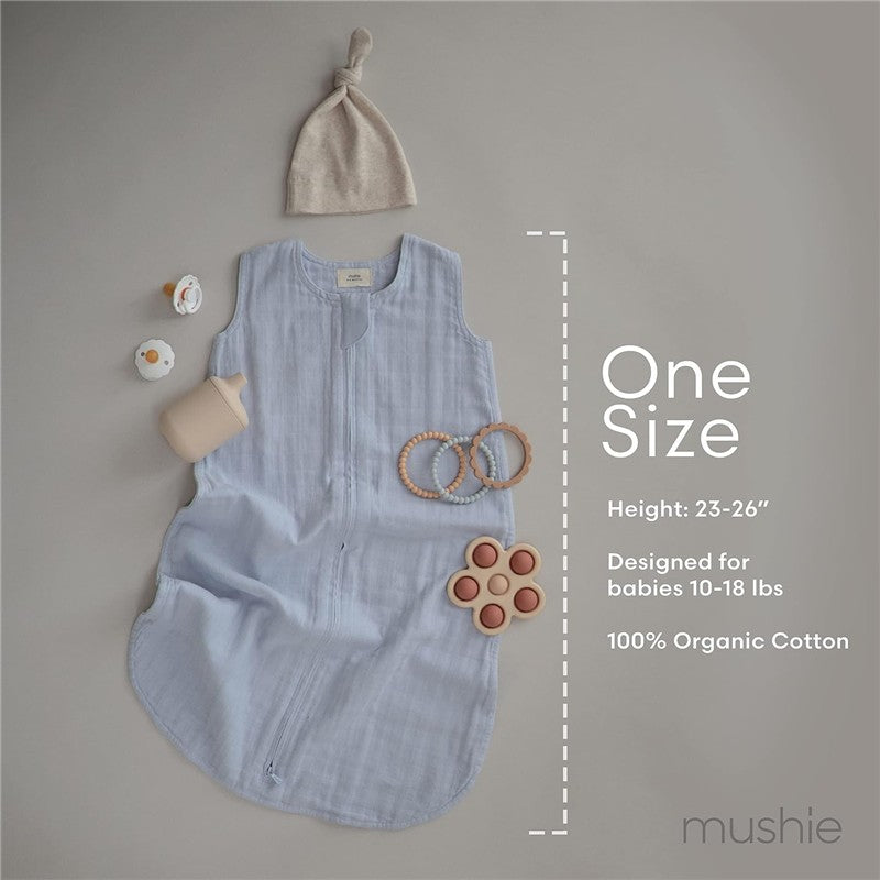 Mushie Muslin Sleep Bag in blush, made of 100% organic cotton, alongside a hat and baby toys, with size and care details.