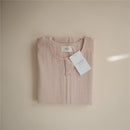 Mushie Muslin Sleep Bag in blush color, neatly folded with a tag attached, showcasing its soft fabric texture.
