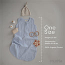 Mushie Muslin Sleep Bag in fog color, made from 100% organic cotton, with a beige knotted hat and baby toys.