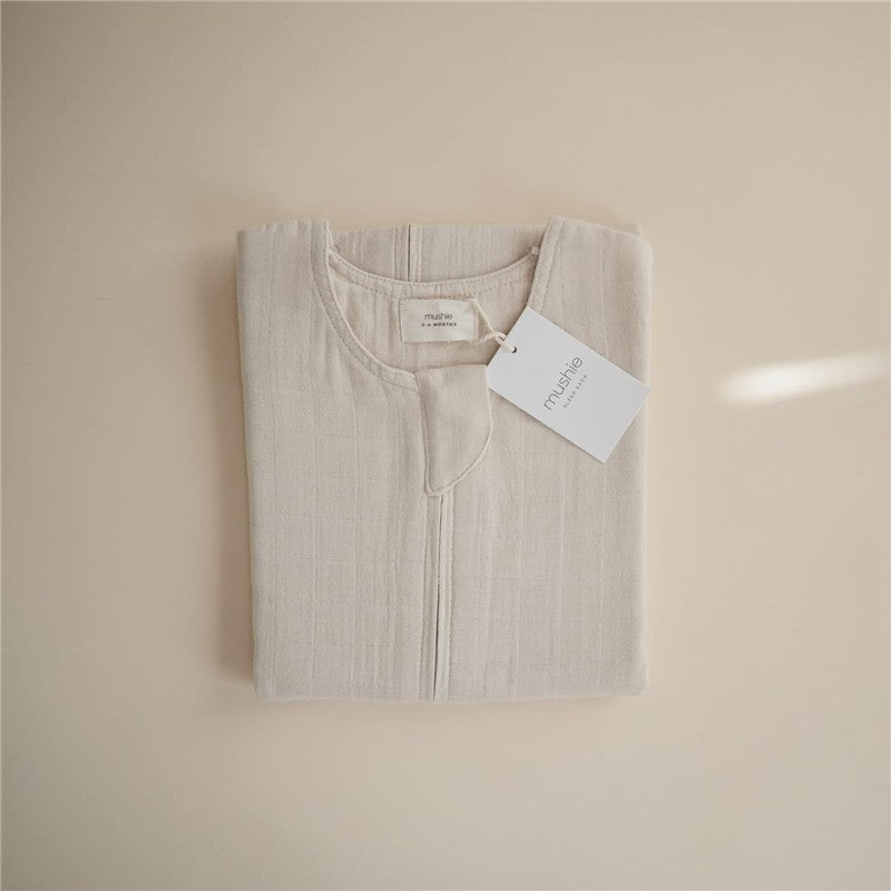 Mushie Muslin Sleep Bag in fog color, neatly folded with a tag displaying the brand name.