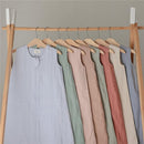 Mushie Muslin Sleep Bags in various colors, displayed on wooden hangers, highlighting their soft fabric and sleeveless design.